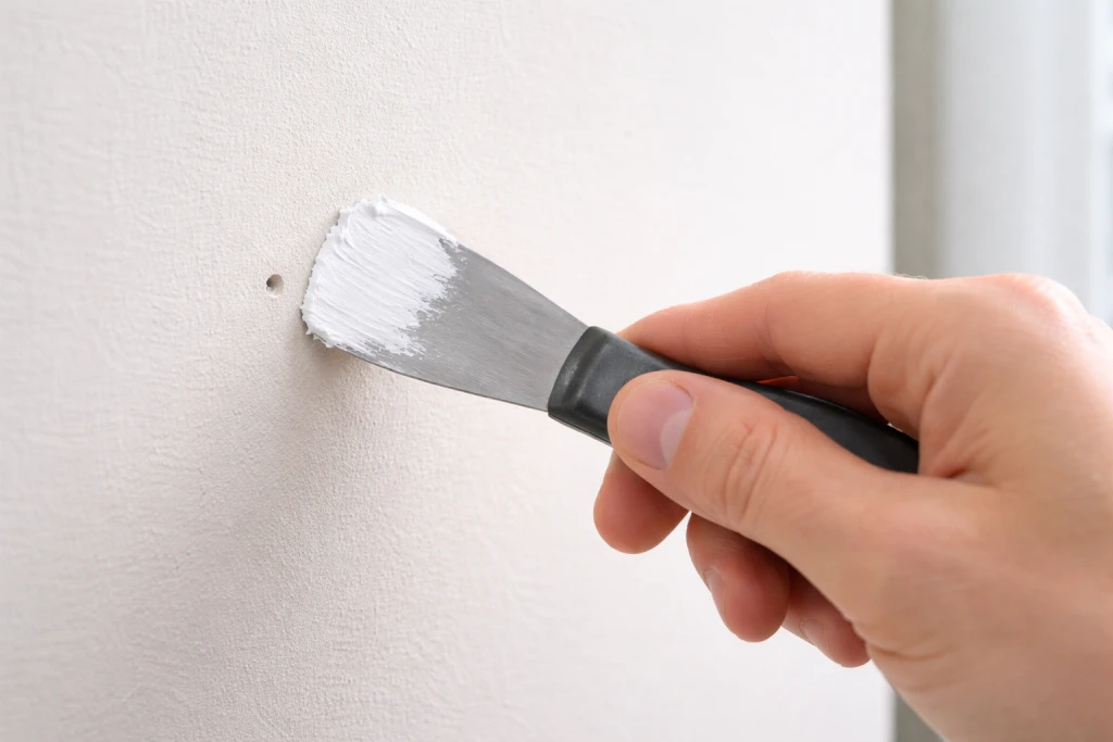 Applying spackle to small nail hole with putty knife for drywall repair