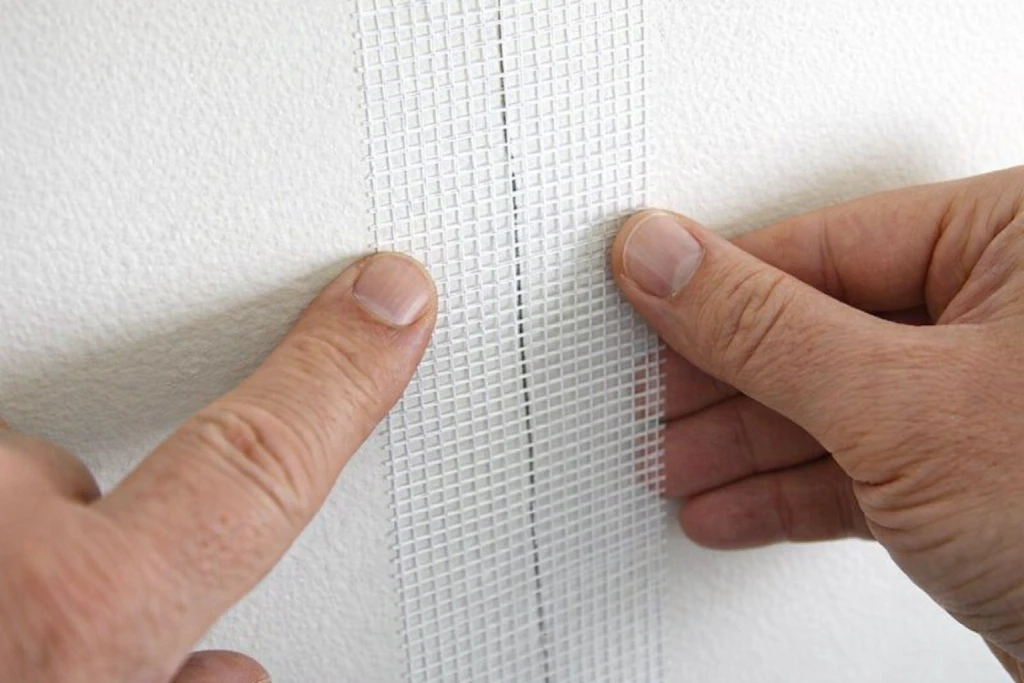 Applying self-adhesive fiberglass mesh tape to drywall patch seams
