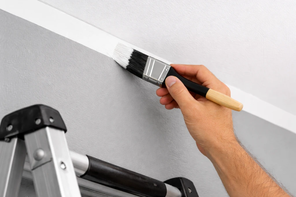 Hand demonstrating cutting in technique painting crisp line where wall meets white ceiling
